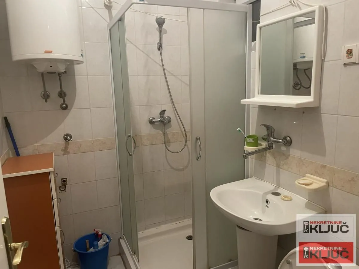 Manje kupatilo sa tuš kabinom, umivaonikom i bojlerom.