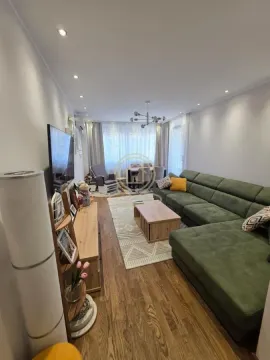 Dnevna soba sa velikom zelenom garniturom, drvenim stočićem i televizorom na zidu. - image 12