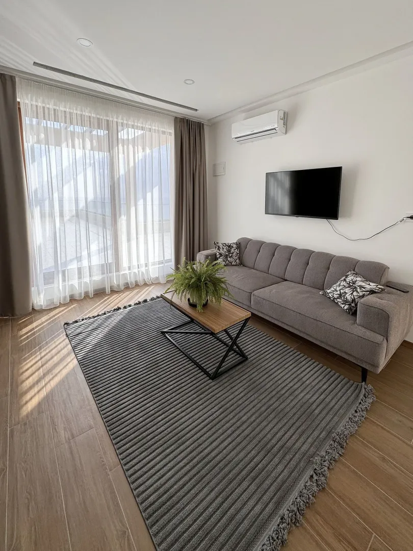 Living room with a grey sofa, coffee table, TV, and access to the terrace.