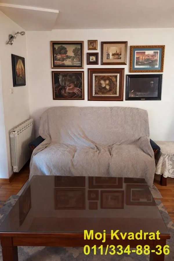 Dnevni boravak sa kaučem prekrivenim prekrivačem i slikama na zidu.