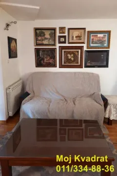 Dnevni boravak sa kaučem prekrivenim prekrivačem i slikama na zidu. - image 4