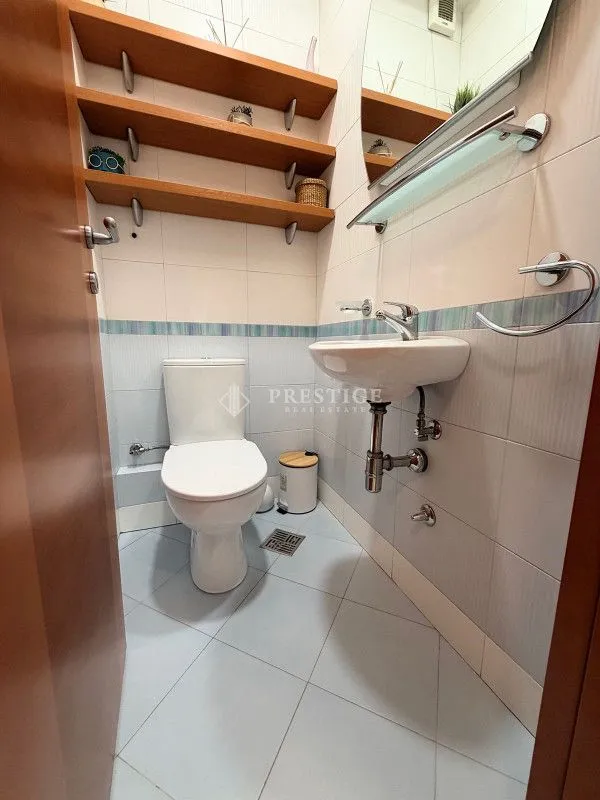 Small bathroom with toilet, washbasin, and wooden wall shelves.
