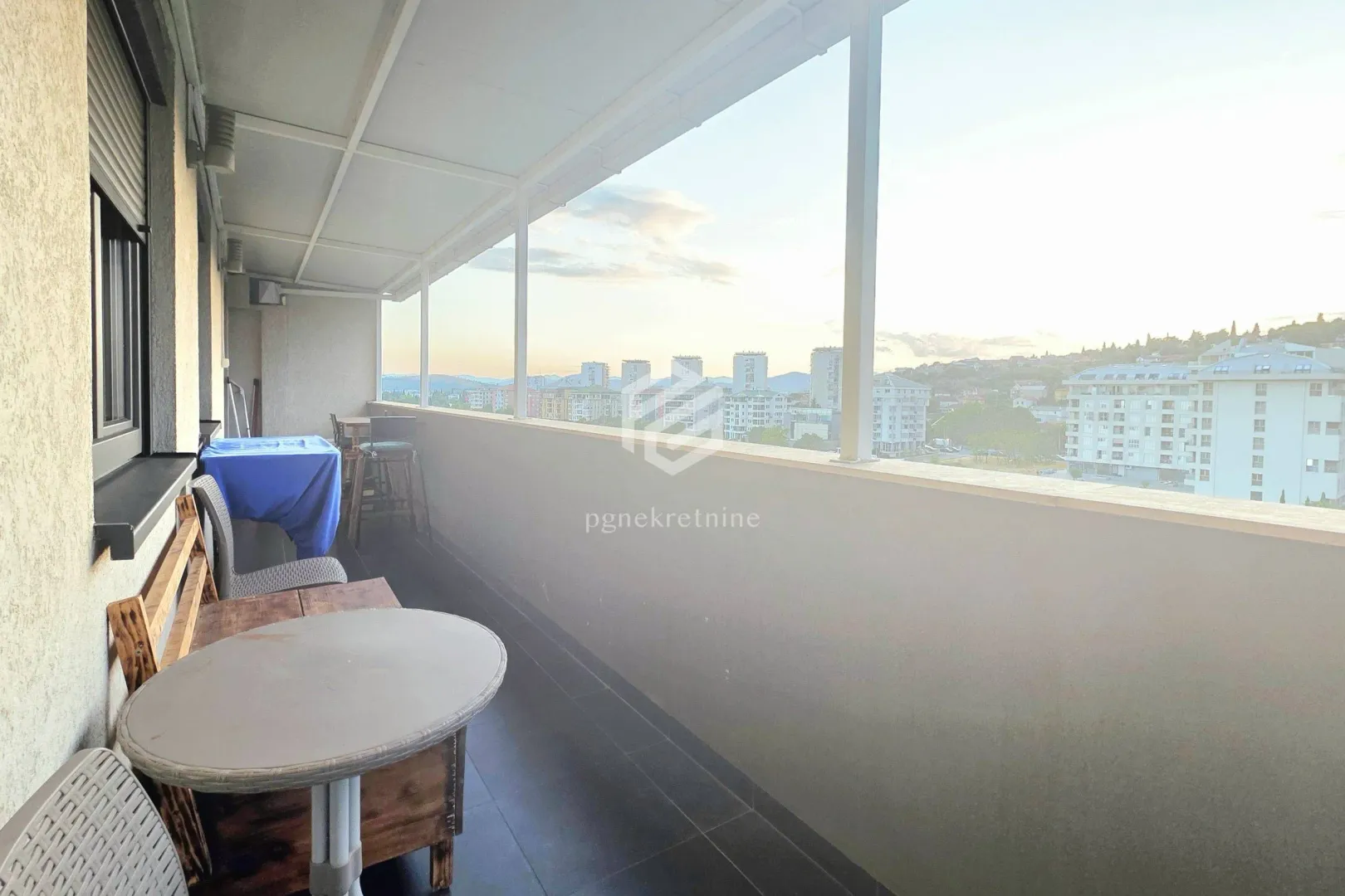 Covered balcony with seating furniture and city view.