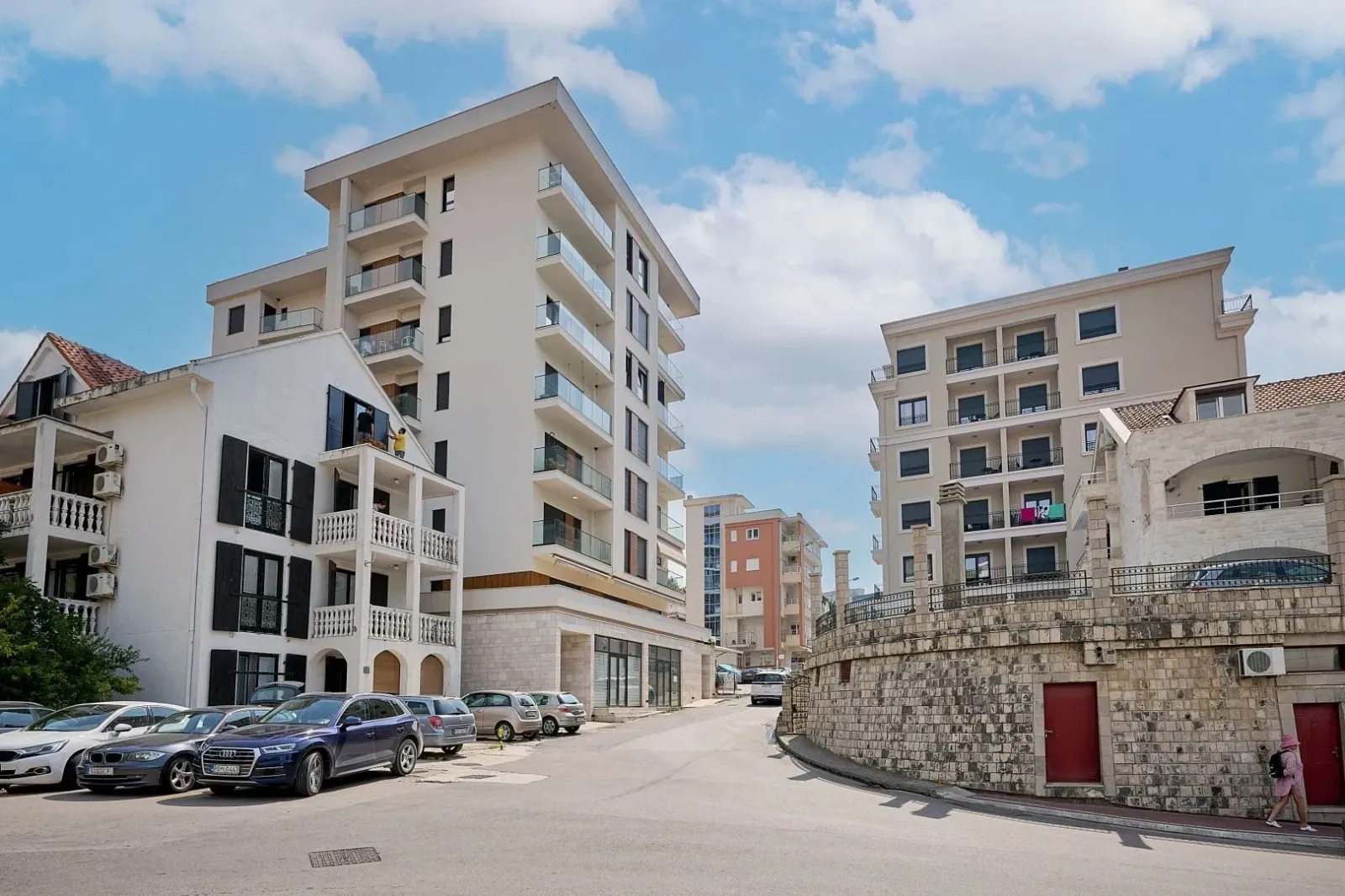 Spoljašnji pogled na moderne stambene zgrade i ulicu sa parkiranim automobilima.
