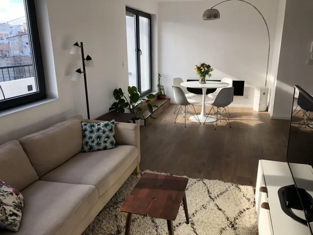 Living room with a sofa, dining table, and windows.