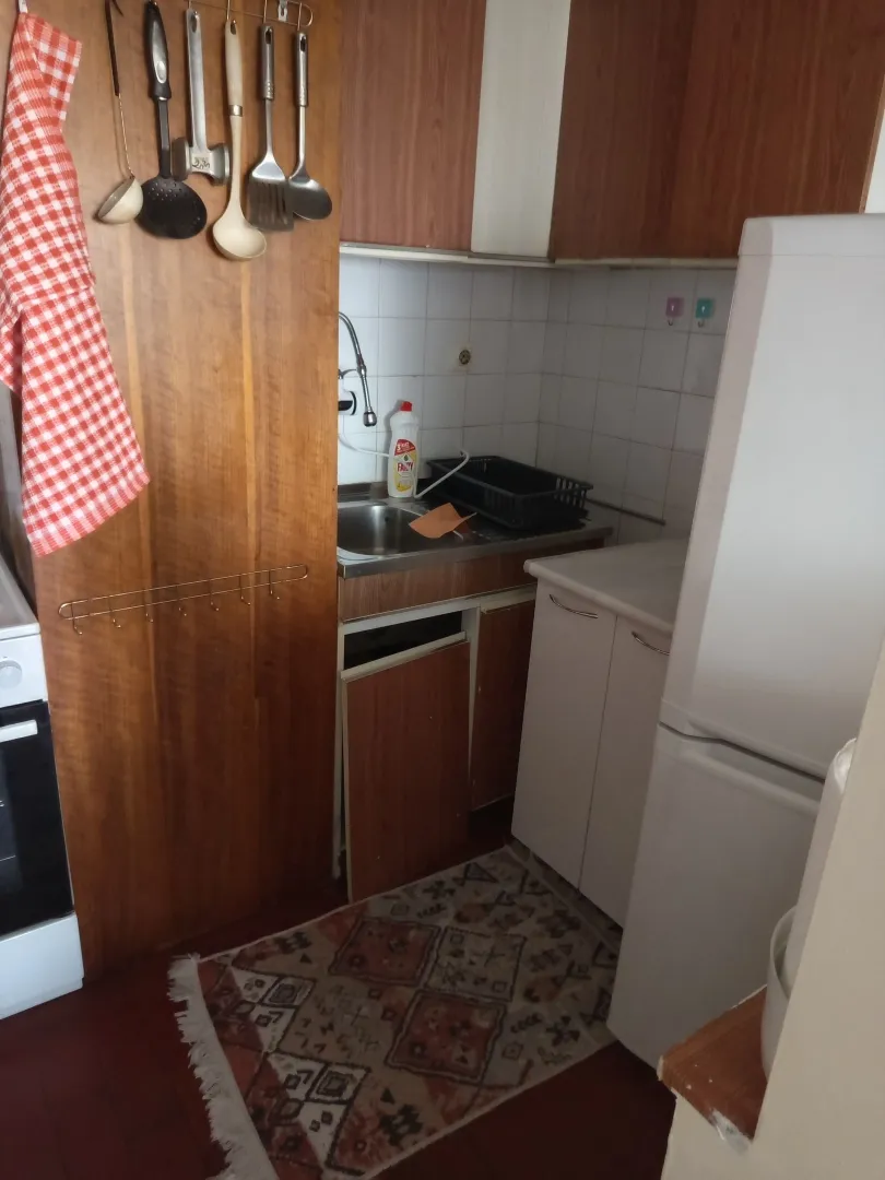 Smaller older kitchen with wooden elements and a refrigerator.