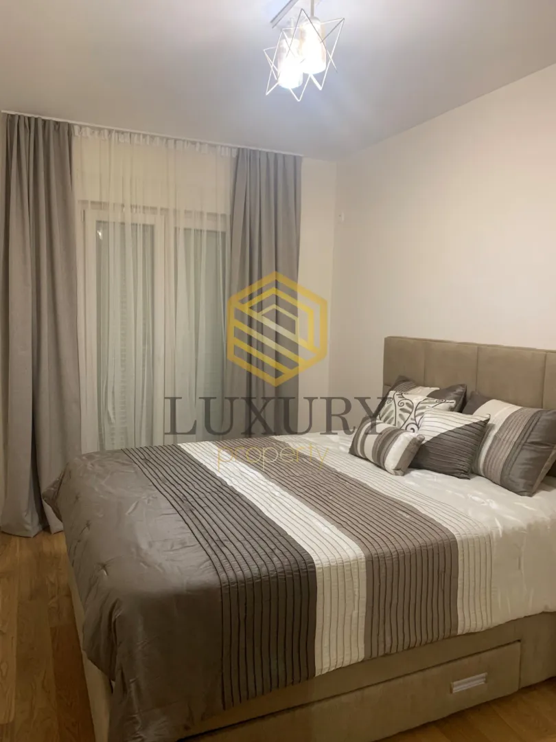 Furnished bedroom with a double bed and a window with curtains.