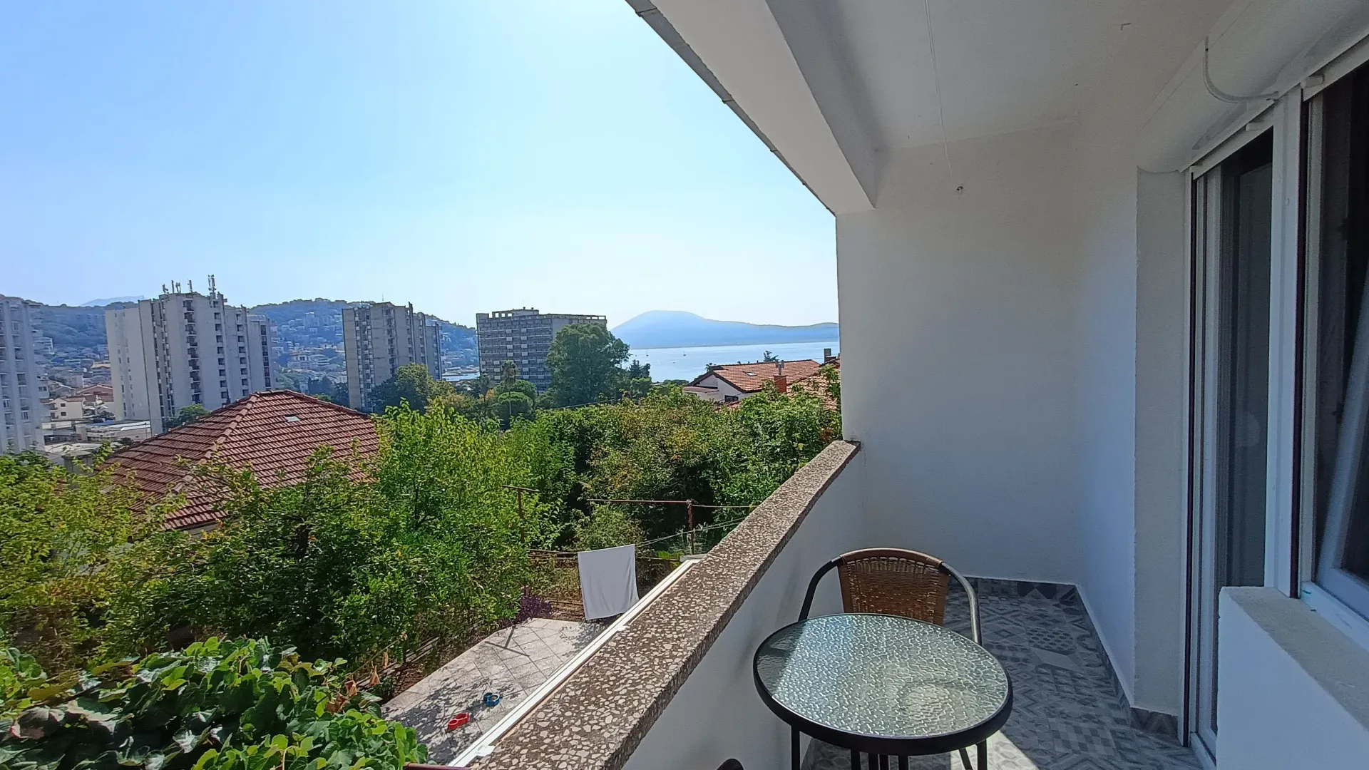 Natkriveni balkon sa garniturom za sjedenje i pogledom na grad i more.