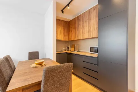 Kuhinja opremljena tamnim elementima i drvenim detaljima sa trpezarijskim stolom. - image 11