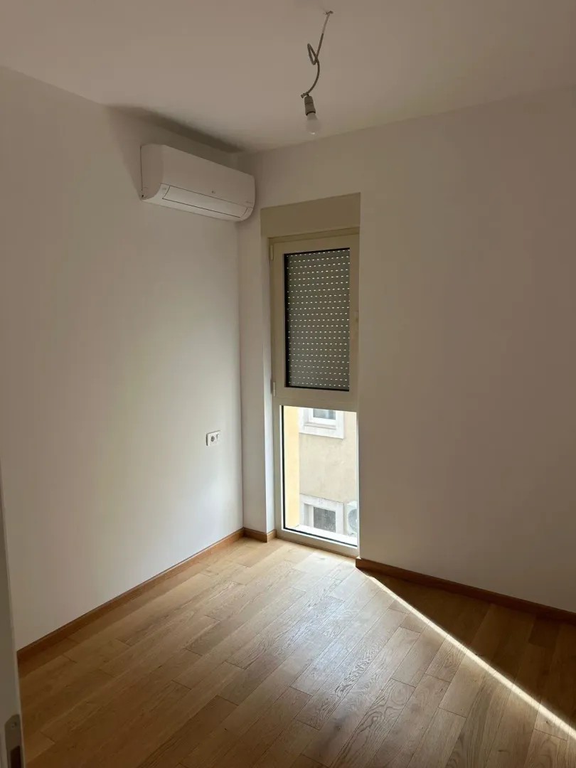 Empty room with wooden flooring, an air conditioning unit, and a window.