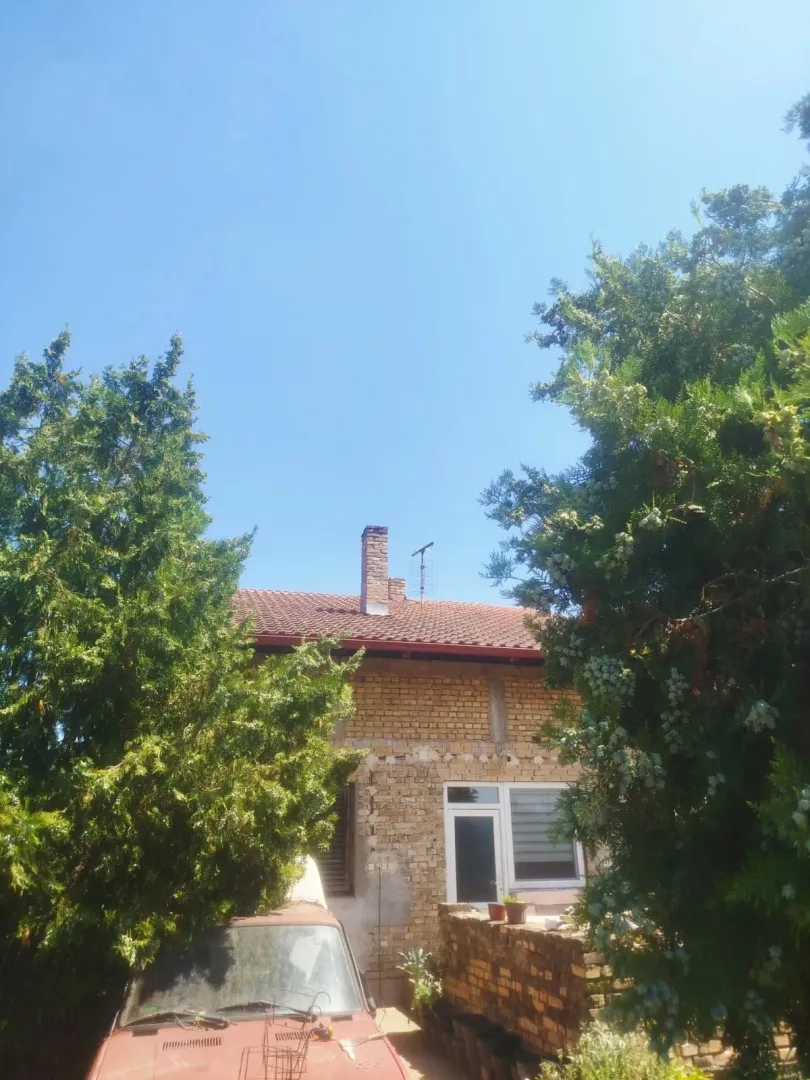 Pogled na deo spoljašnjosti kuće sa drvećem u dvorištu.