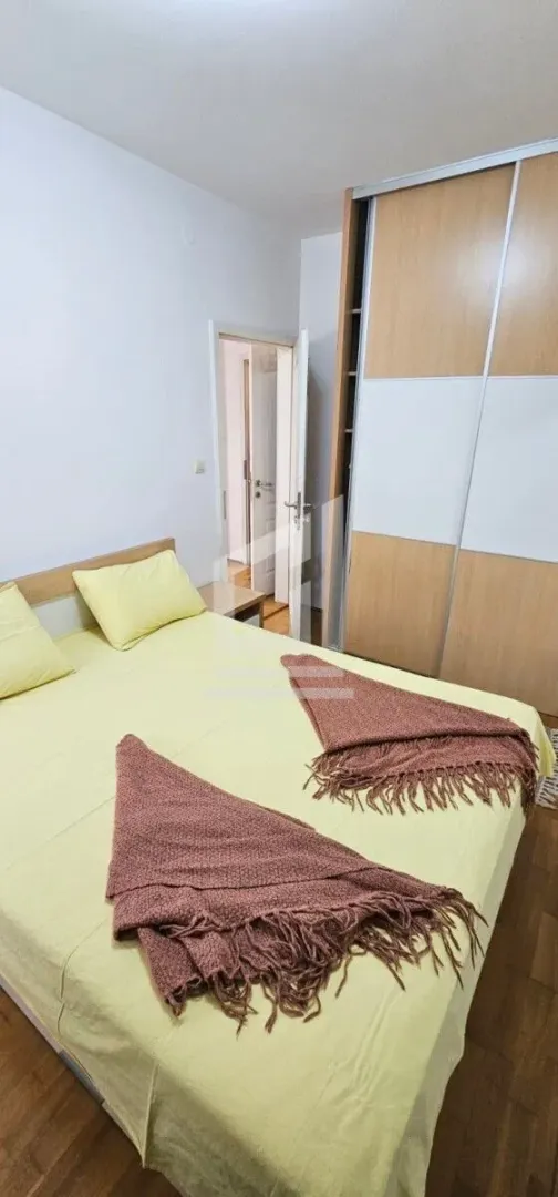 Namještena spavaća soba sa bračnim krevetom i ugradnim plakarom.