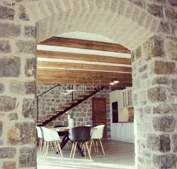 View through a stone archway into the living room with a dining area and exposed wooden ceiling beams. - image 6