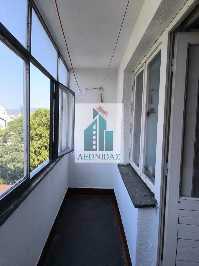 Zastakljeni balkon sa prozorima i pogledom na zelenilo.