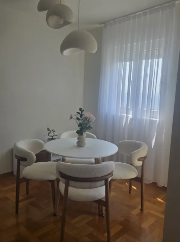 Trpezarija sa okruglim stolom i modernim stolicama pored prozora.