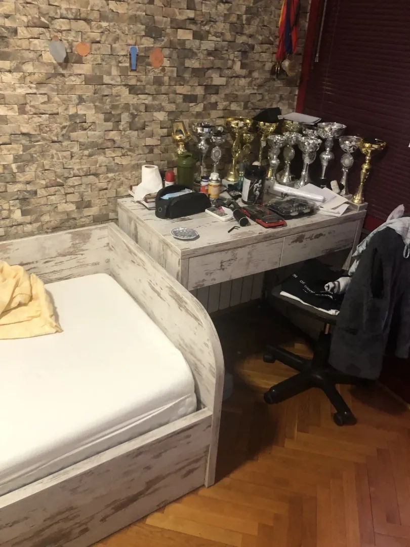 Dječija soba sa drvenim krevetom, radnim stolom i dekorativnim kamenim zidom.