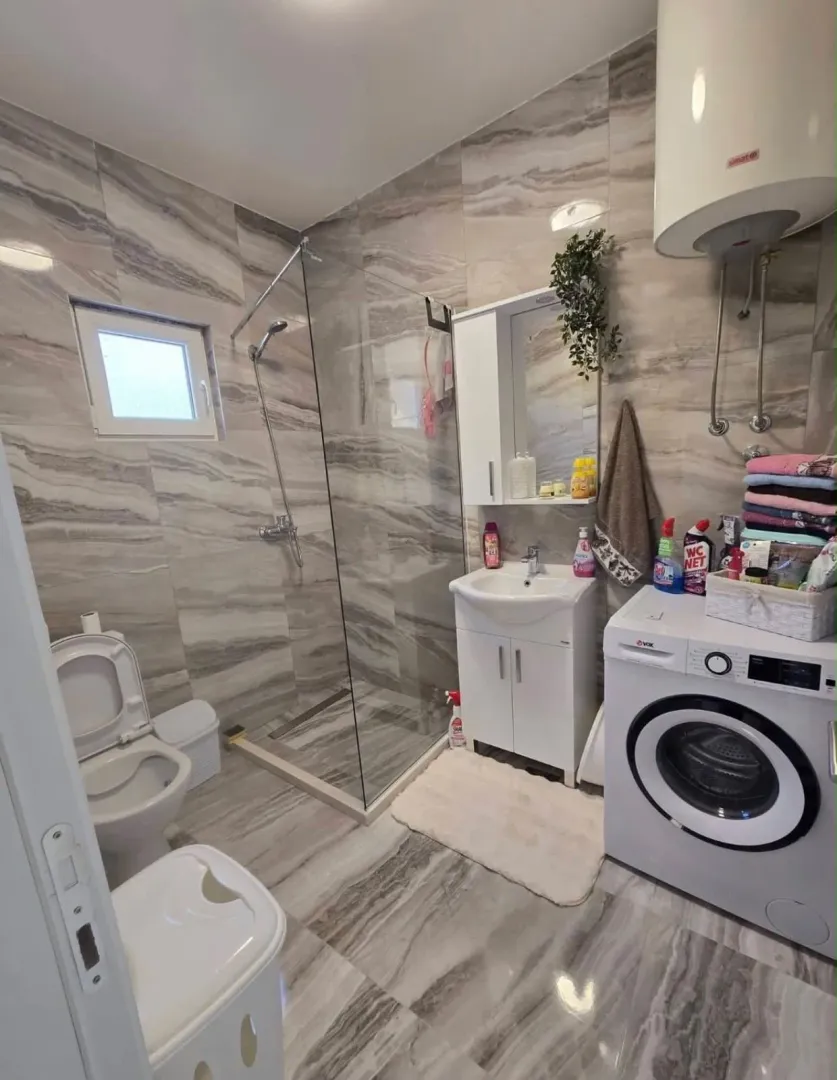 Modern bathroom with a walk-in shower, washbasin, and washing machine.