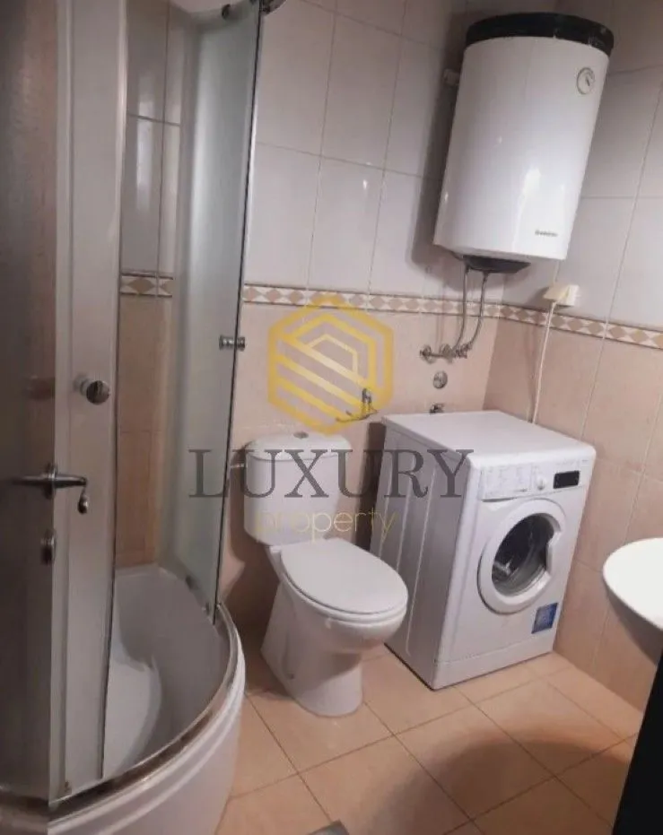 Smaller bathroom with a shower cabin, toilet, and washing machine.
