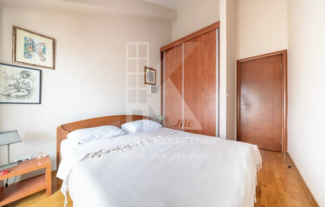 Furnished bedroom with a double bed, wooden wardrobe, and parquet flooring.