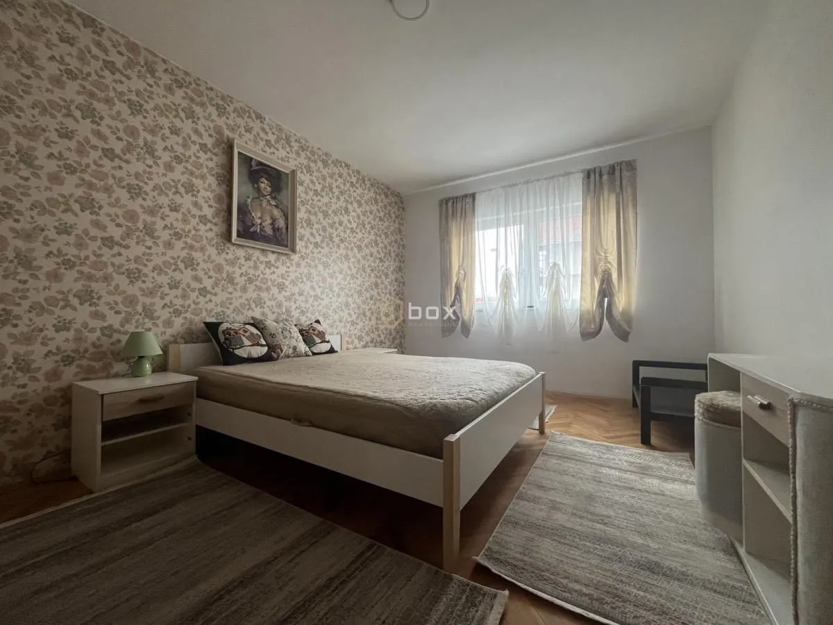 Furnished bedroom with a double bed, bedside table, and patterned wallpaper on the wall.