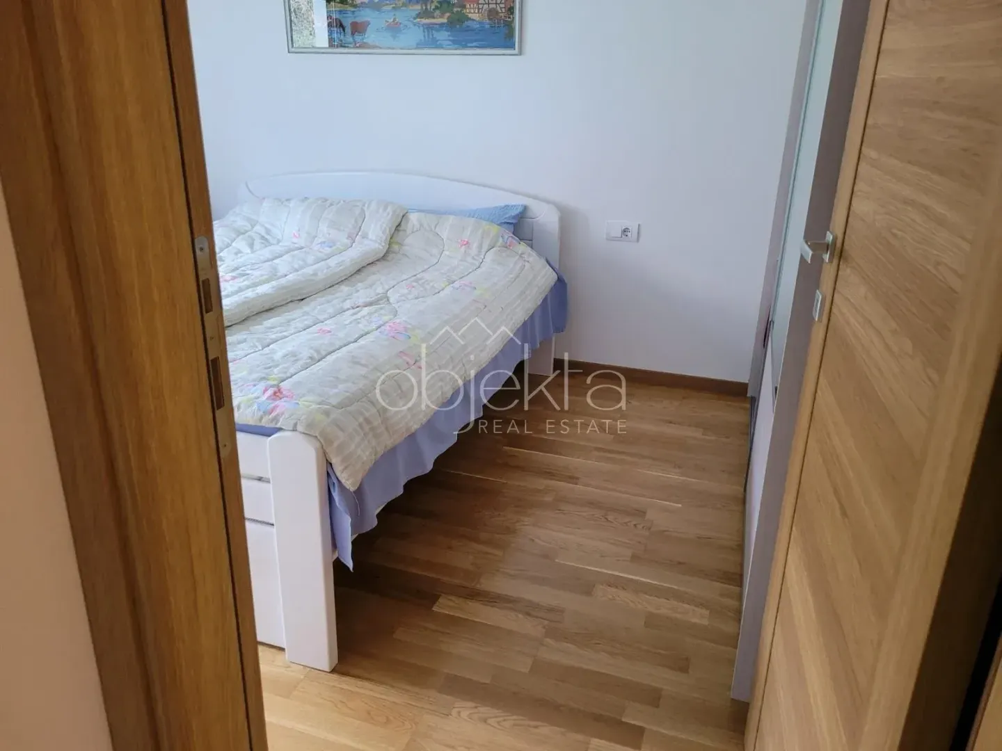 Pogled na spavaću sobu sa krevetom i drvenim podom.