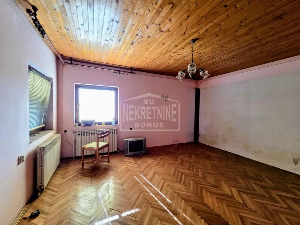 Prazna prostorija sa drvenim podom, drvenim plafonom i radijatorom.