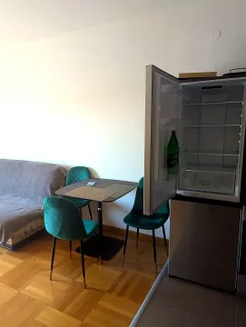 Small kitchen with an open refrigerator and a dining table with green chairs. - image 2
