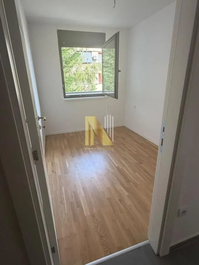Prazna soba sa parketom i otvorenim prozorom.