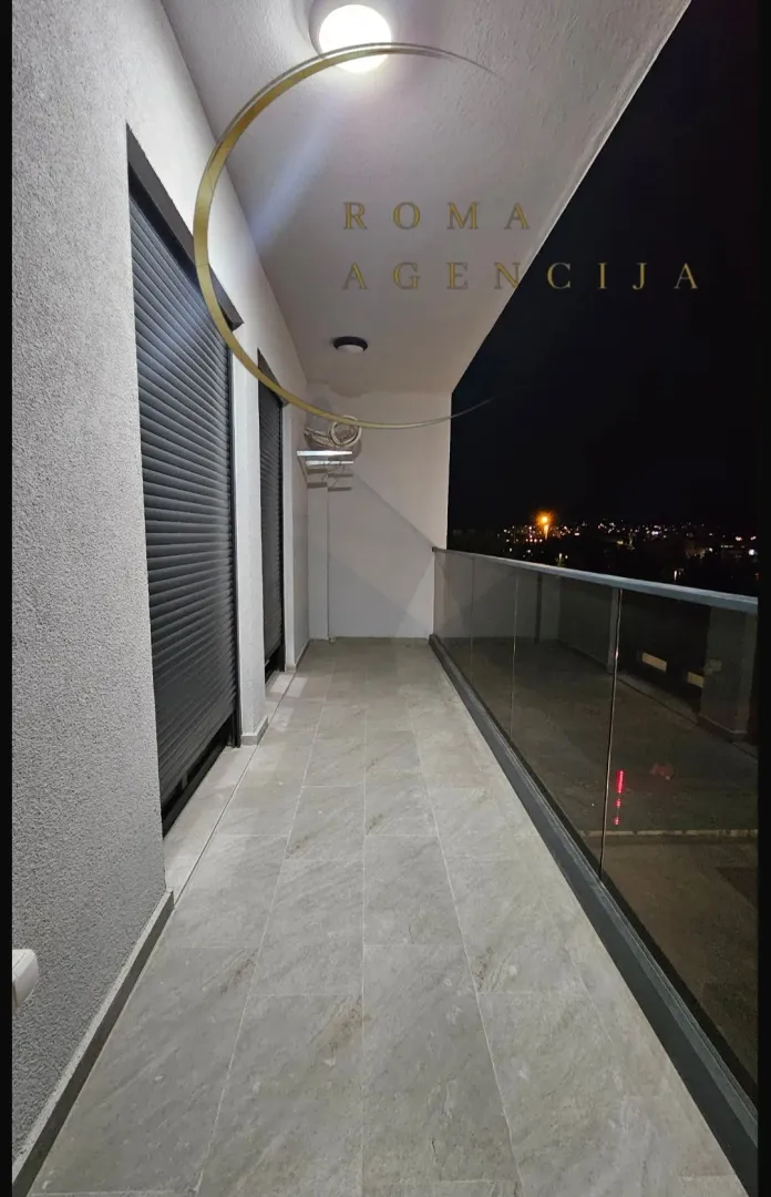 Osvijetljena terasa sa staklenom ogradom i pogledom na grad noću.