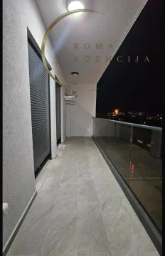 Osvijetljena terasa sa staklenom ogradom i pogledom na grad noću. - image 10