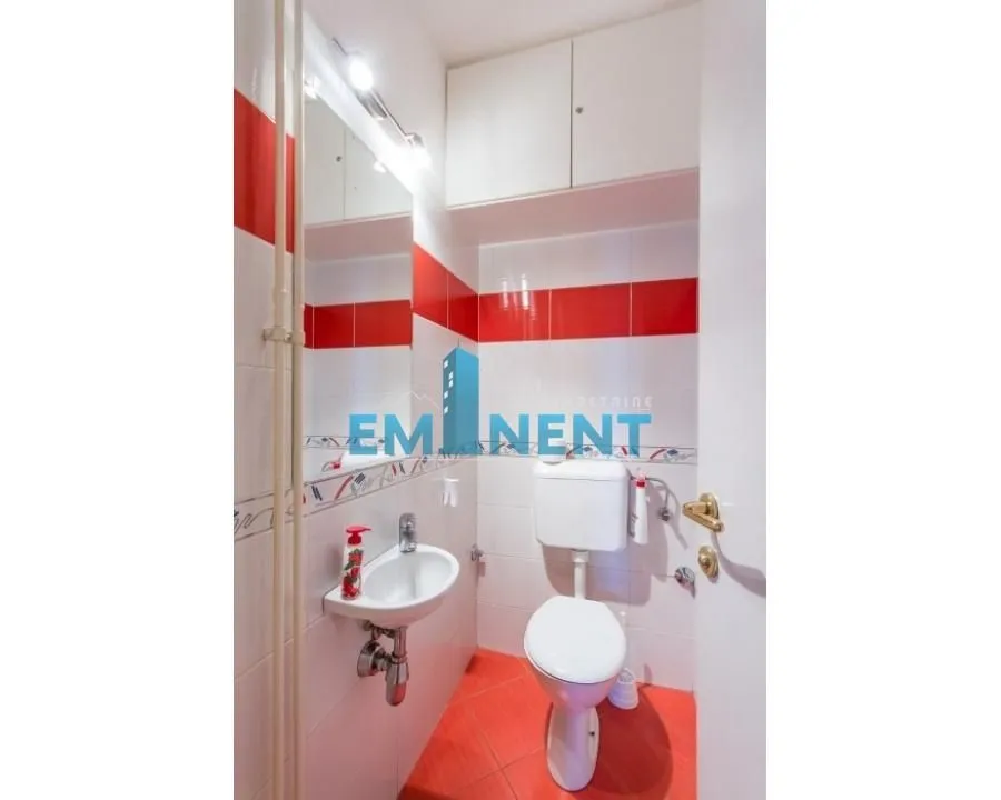 Small bathroom with white tiles, red details, and basic sanitary fixtures.