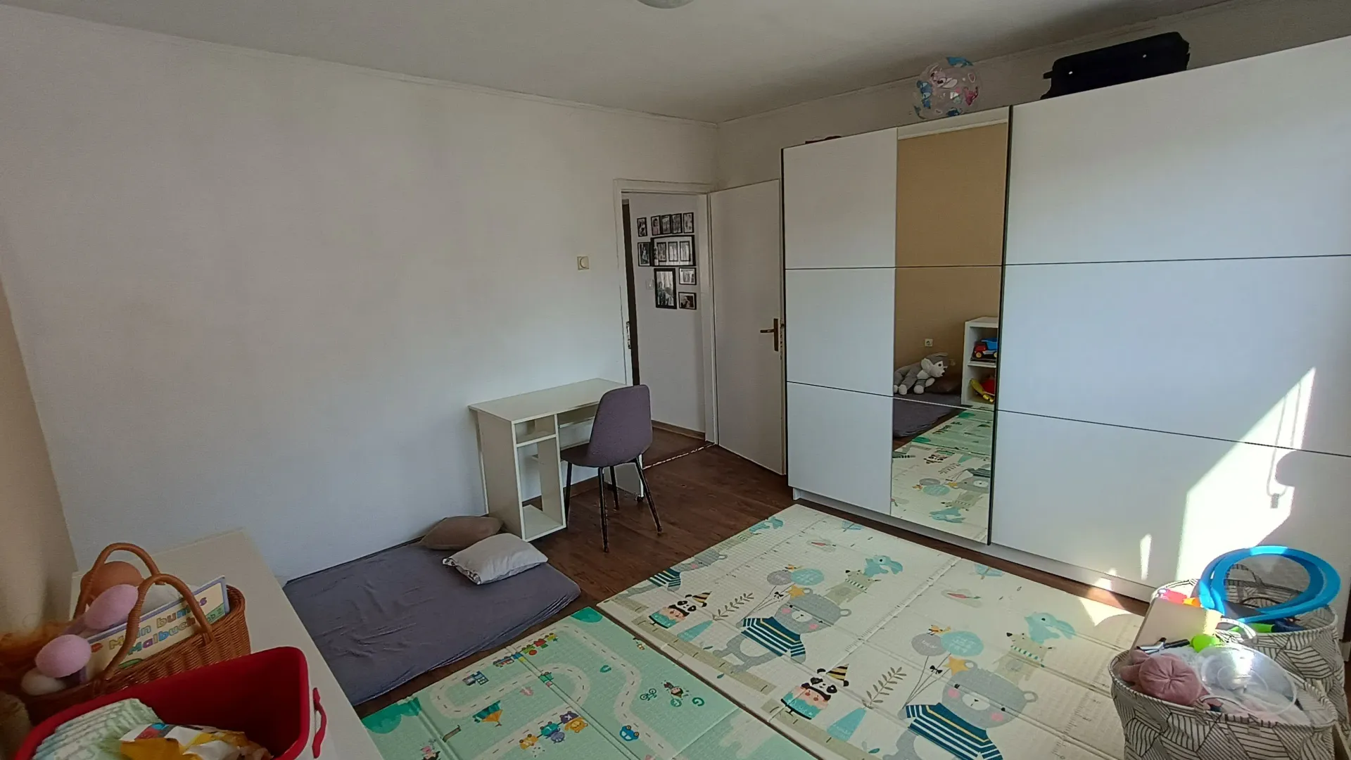 Dječja soba sa krevetom na podu, velikim bijelim ormarom i radnim stolom.