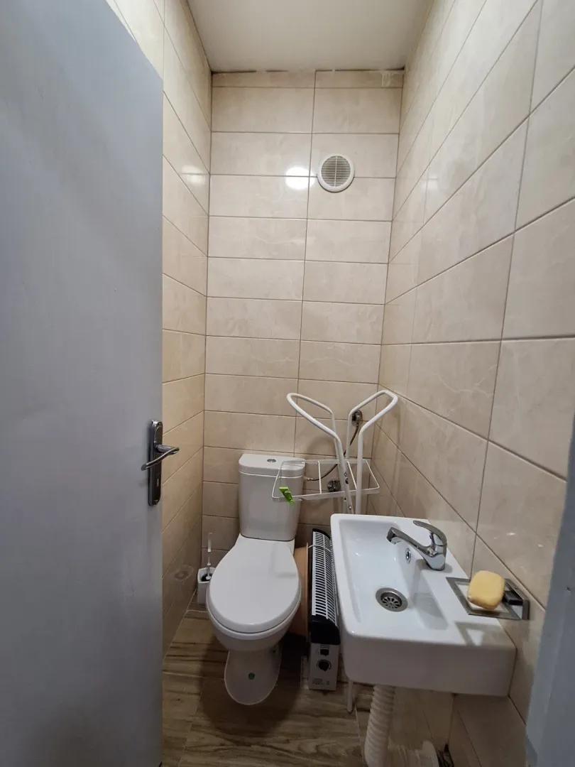 Manje kupatilo sa wc šoljom, umivaonikom i pločicama na zidovima.