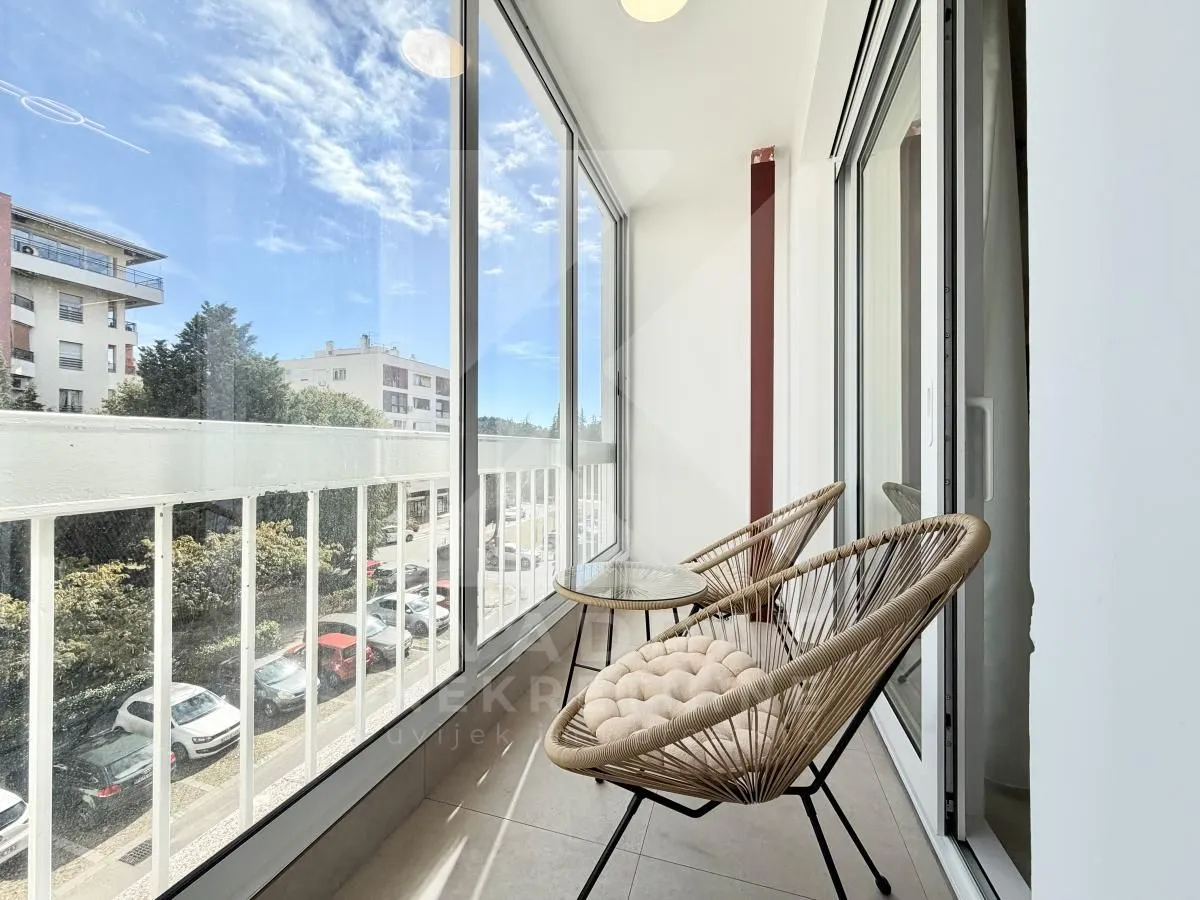 Zastakljeni balkon sa stolicama i pogledom na ulicu.