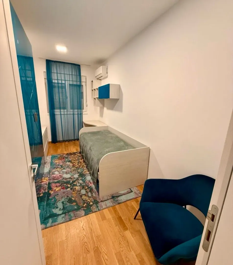 Dječija soba sa krevetom, plavom foteljom i šarenim tepihom.
