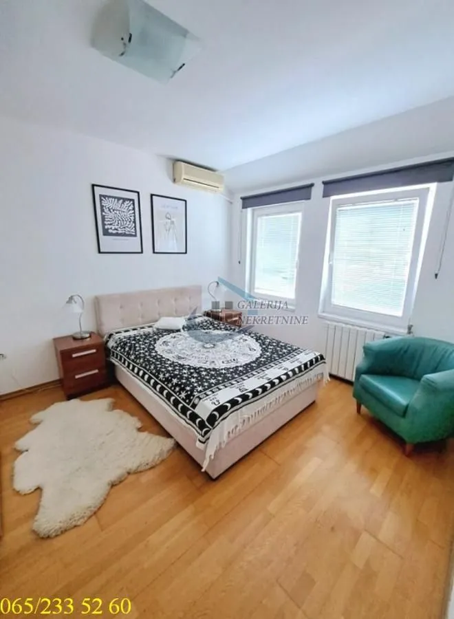 Nameštena spavaća soba sa bračnim krevetom, foteljom i prozorima.