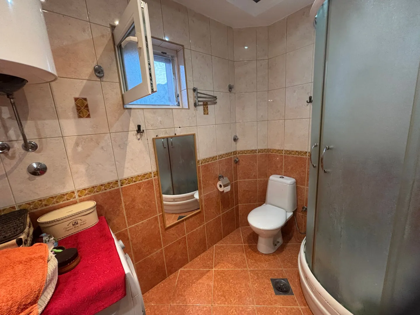 Manje kupatilo sa tuš kabinom, WC šoljom i pločicama u braon tonovima.