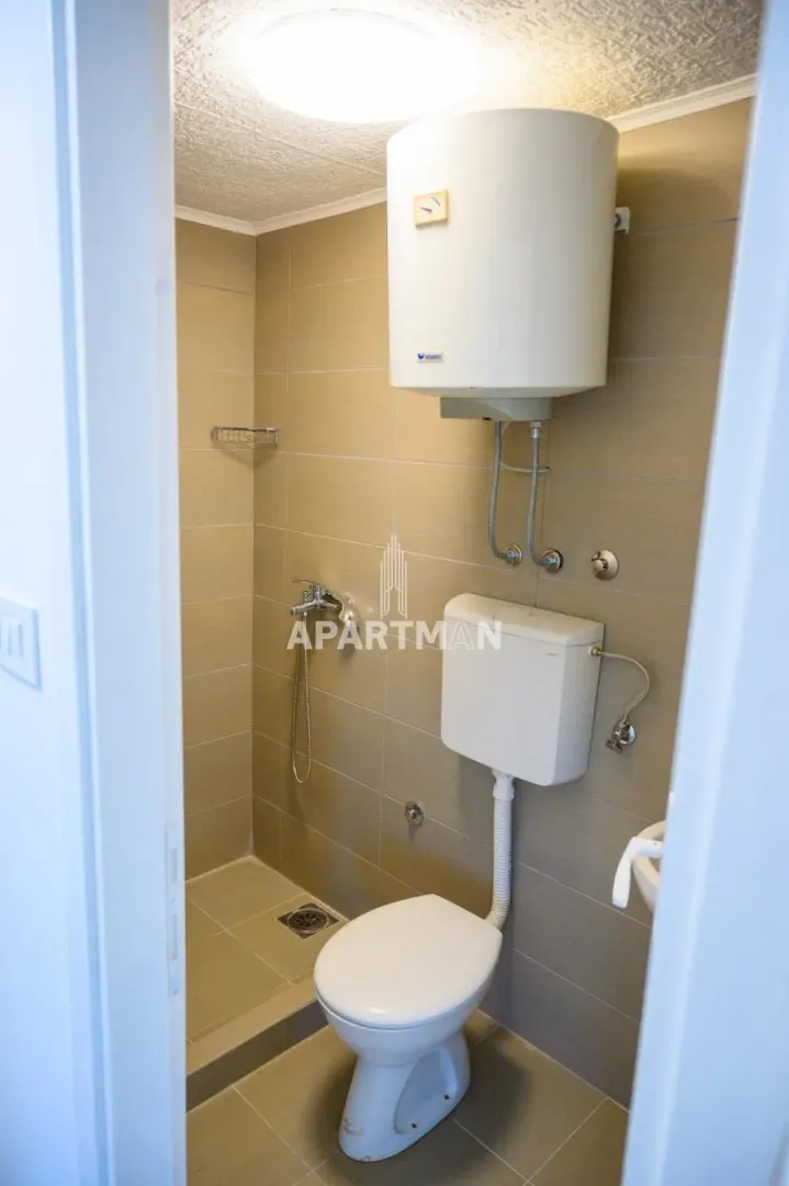 Pogled na manje kupatilo sa tuš kabinom, WC šoljom i bojlerom.
