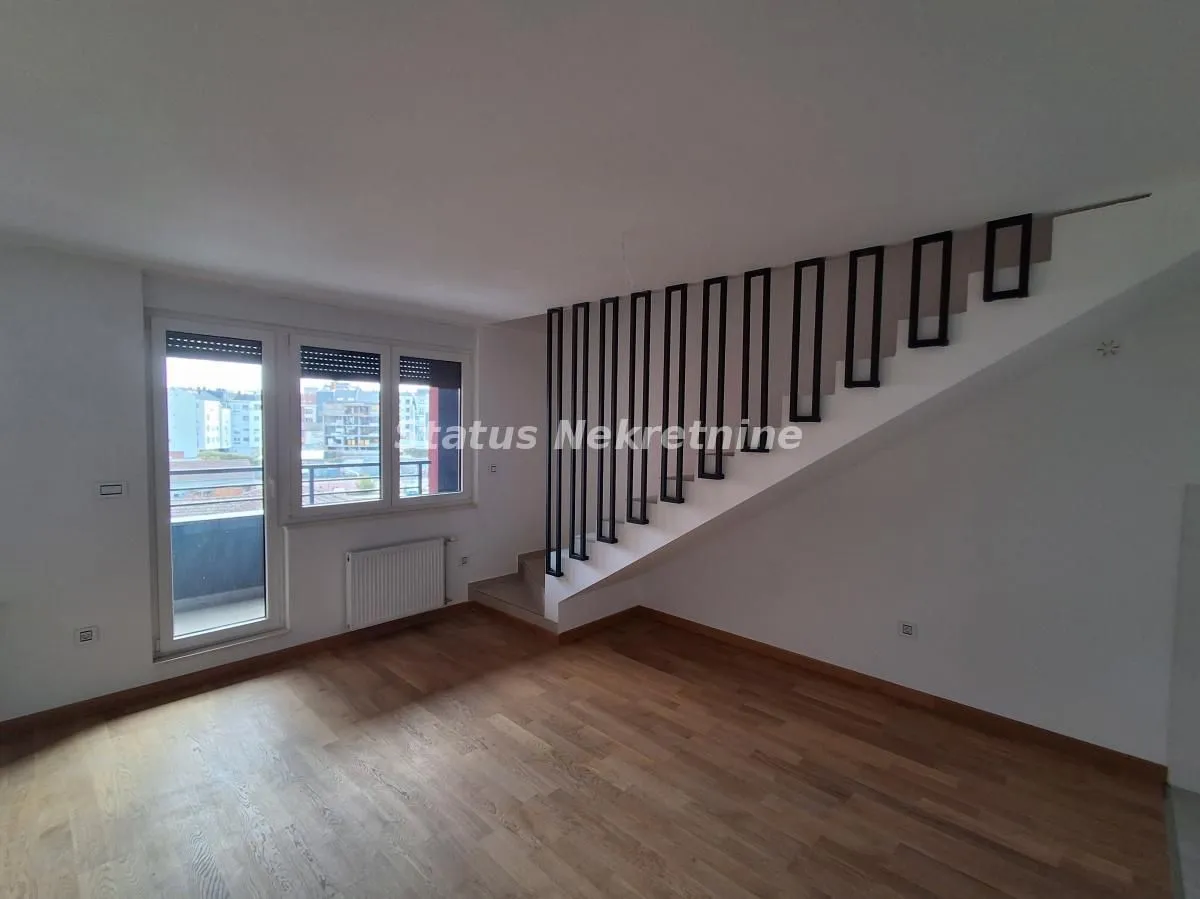 Prazna dnevna soba sa stepeništem i izlazom na balkon.