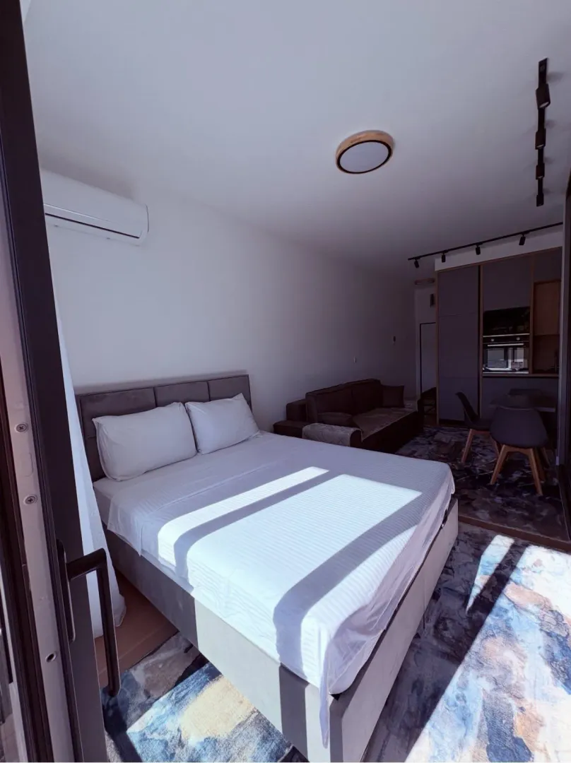 Modern bedroom with a double bed and a view towards the kitchen and living area.