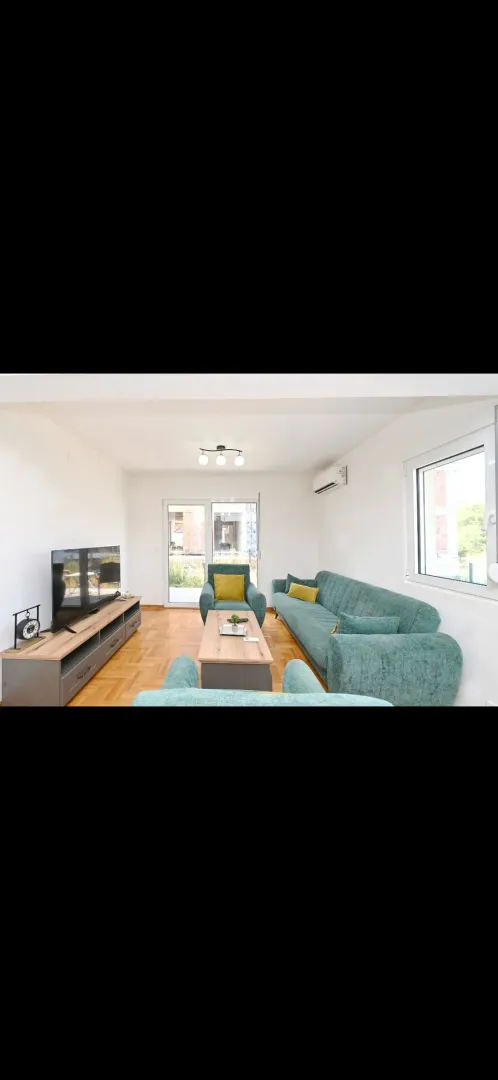 Bright living room with sofa set, television, and parquet flooring.