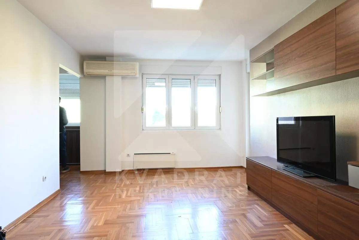 Living room with hardwood flooring, TV unit, and air conditioning.