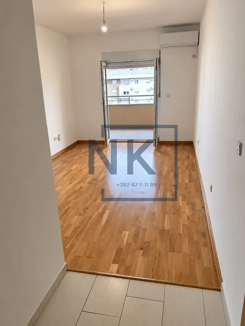 Prazna soba sa drvenim parketom i izlazom na balkon.