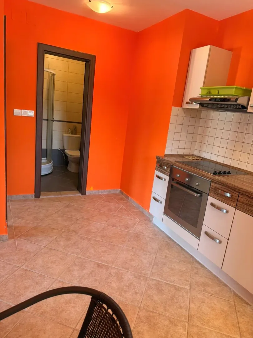 Manja kuhinja sa belim elementima i narandžastim zidovima.
