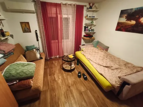 Dnevna soba sa krevetom, sofom, stočićem i prozorom sa crvenim zavjesama. - image 7