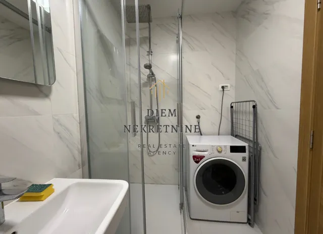 Moderne kupatilo sa tuš kabinom, umivaonikom i mašinom za veš.