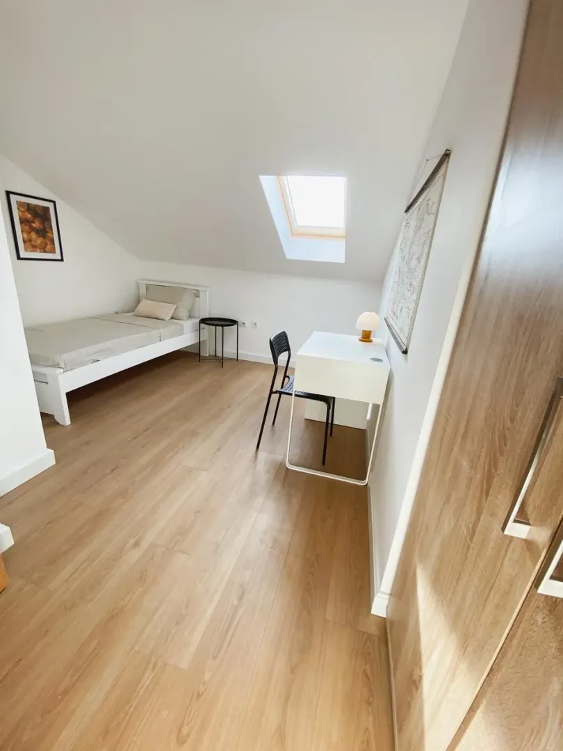 Attic bedroom with a bed, desk, and a roof window.