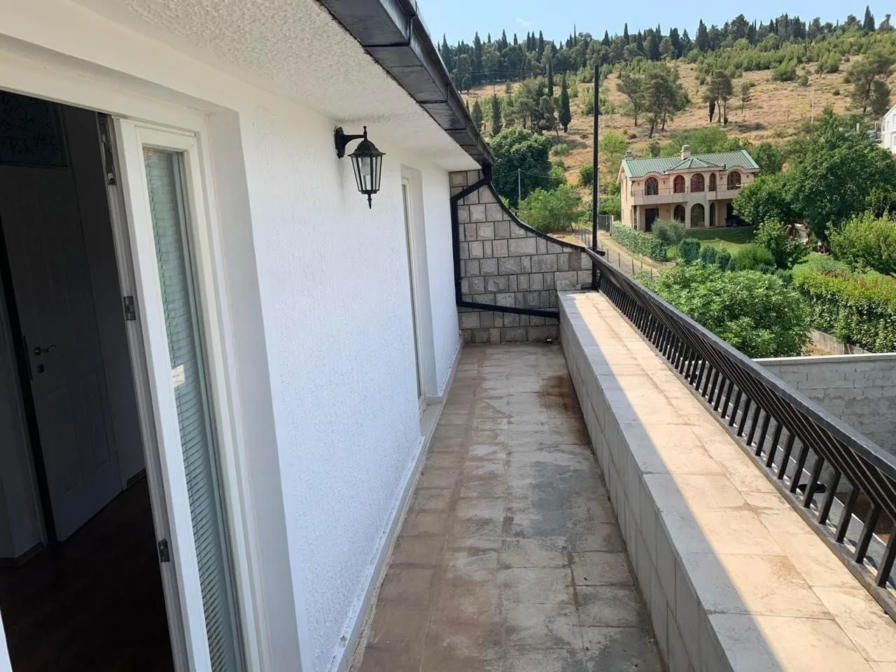 A long balcony with a railing and views of the green hillside.