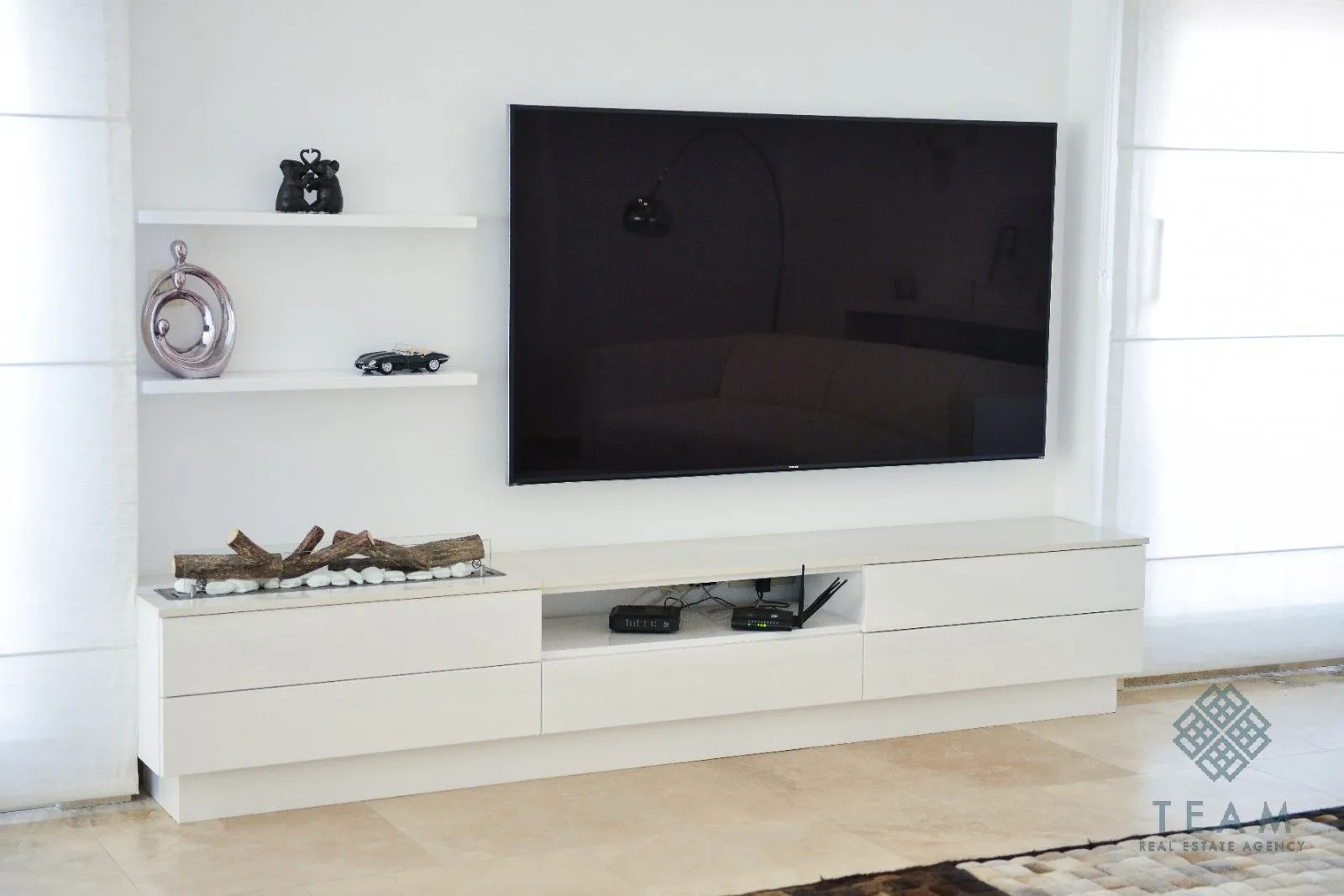 Moderna TV komoda sa velikim televizorom i ukrasnim detaljima na zidu.