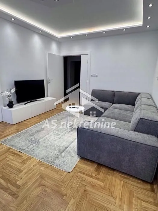 Dnevni boravak sa garniturom, televizorom i parketom na podu.